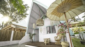 A covered outdoor area with a wooden deck, wicker furniture, and a large umbrella. - 7SEAS Cottages (Gili Air)