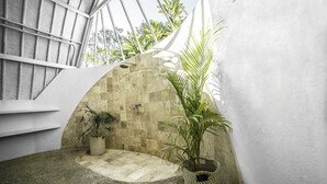 A modern interior with a curved stone wall, a small seating area, and a potted plant. - 7SEAS Cottages (Gili Air)