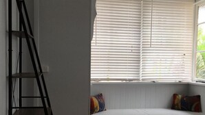 A room with a wooden floor, a white bench with colorful cushions, and a window with white blinds. - Cairns City Backpackers Hostel (Parramatta Park)