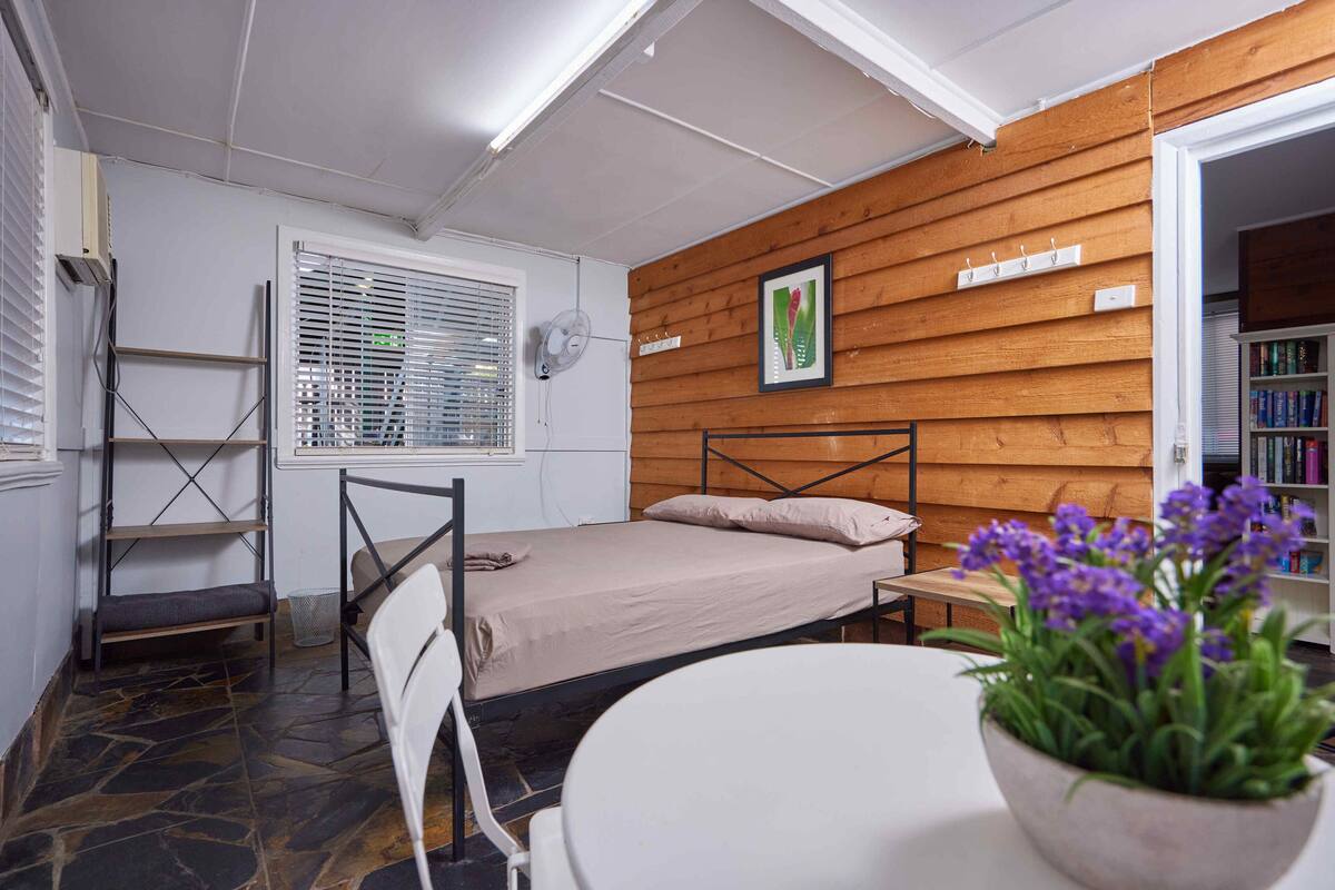 A small, cozy room with a single bed, a chair, a table, and a potted plant.