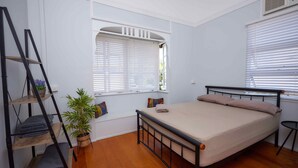A bedroom with a bed, a window with blinds, a shelf with folded towels, a potted plant, and a ladder. - Cairns City Backpackers Hostel (Parramatta Park)