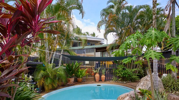 A swimming pool surrounded by tropical plants and a house in the background. - Cairns City Backpackers Hostel (Parramatta Park)