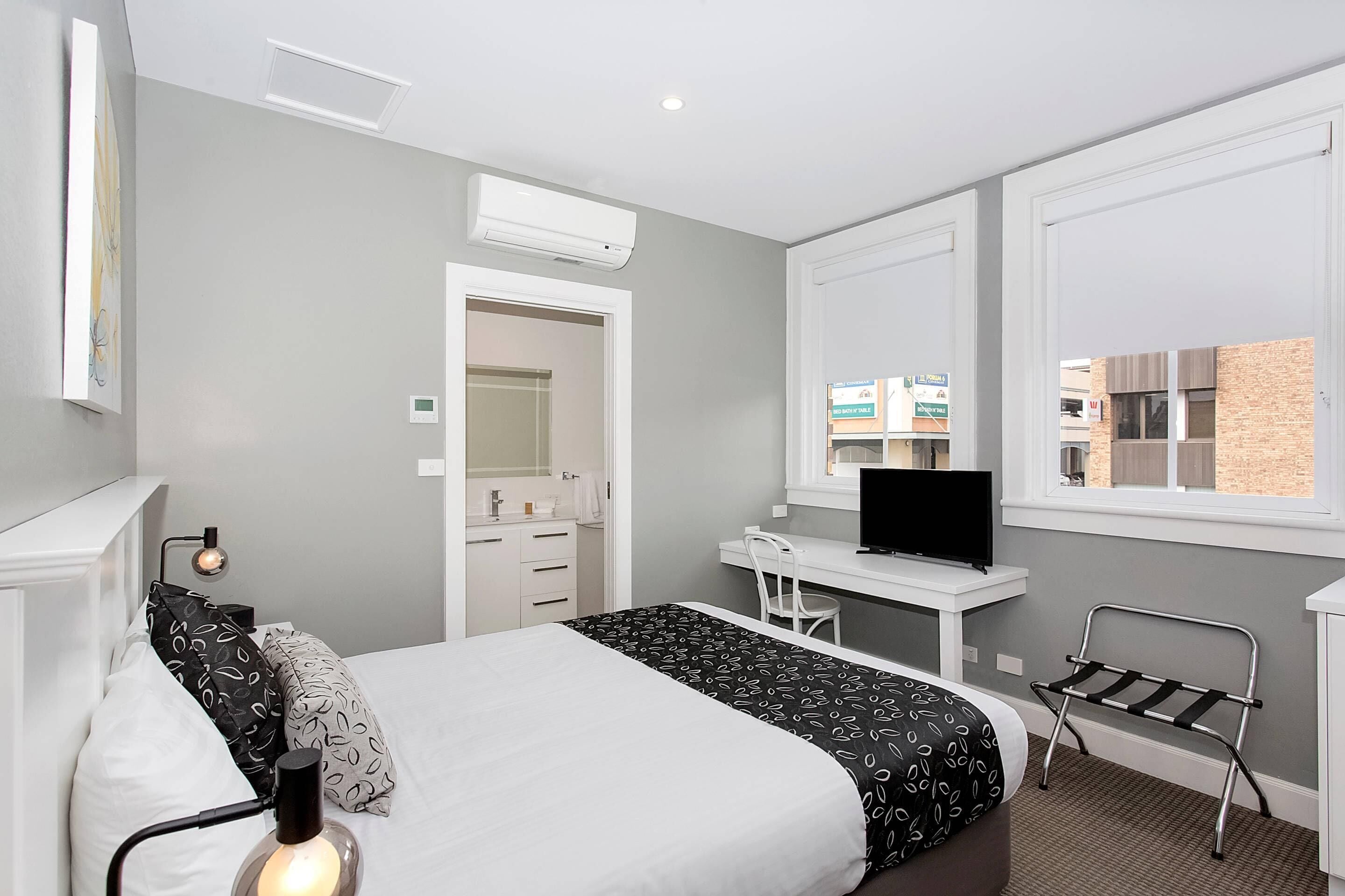 Habitación de hotel con cama, escritorio, televisión y ventana con vistas a edificios.