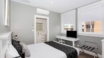 Habitación de hotel con cama, escritorio, televisión y ventana con vistas a edificios.