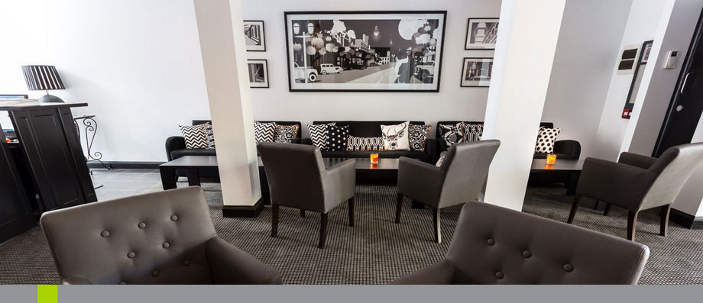 A modern lounge area with a sofa and chairs, a coffee table, and a framed cityscape picture on the wall.