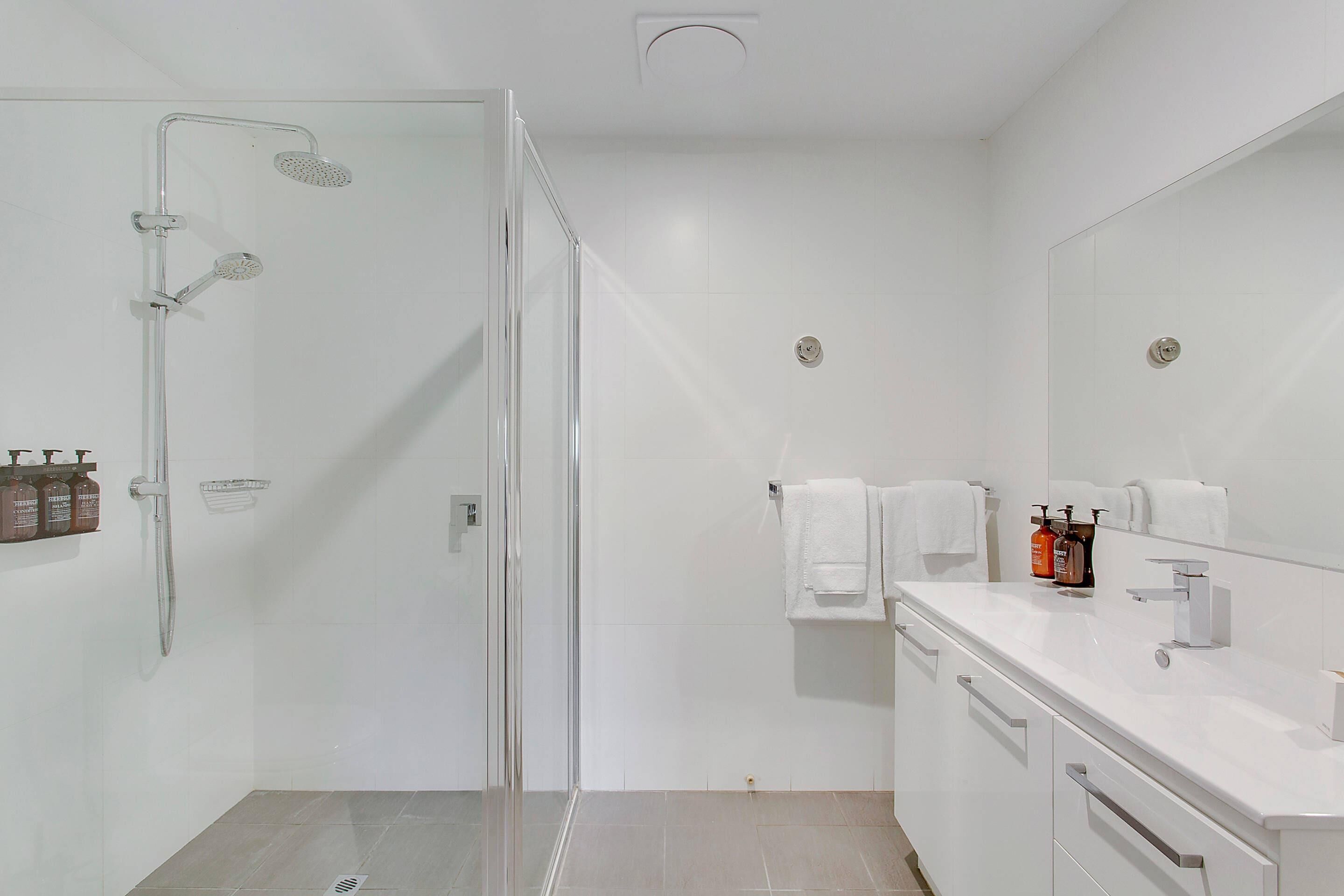 A modern bathroom with a glass shower enclosure, a white vanity with a mirror, and toiletries on the counter.