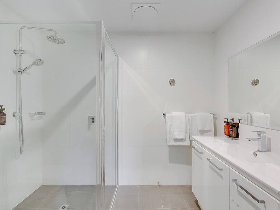 A modern bathroom with a glass shower enclosure, a white vanity with a mirror, and toiletries on the counter.