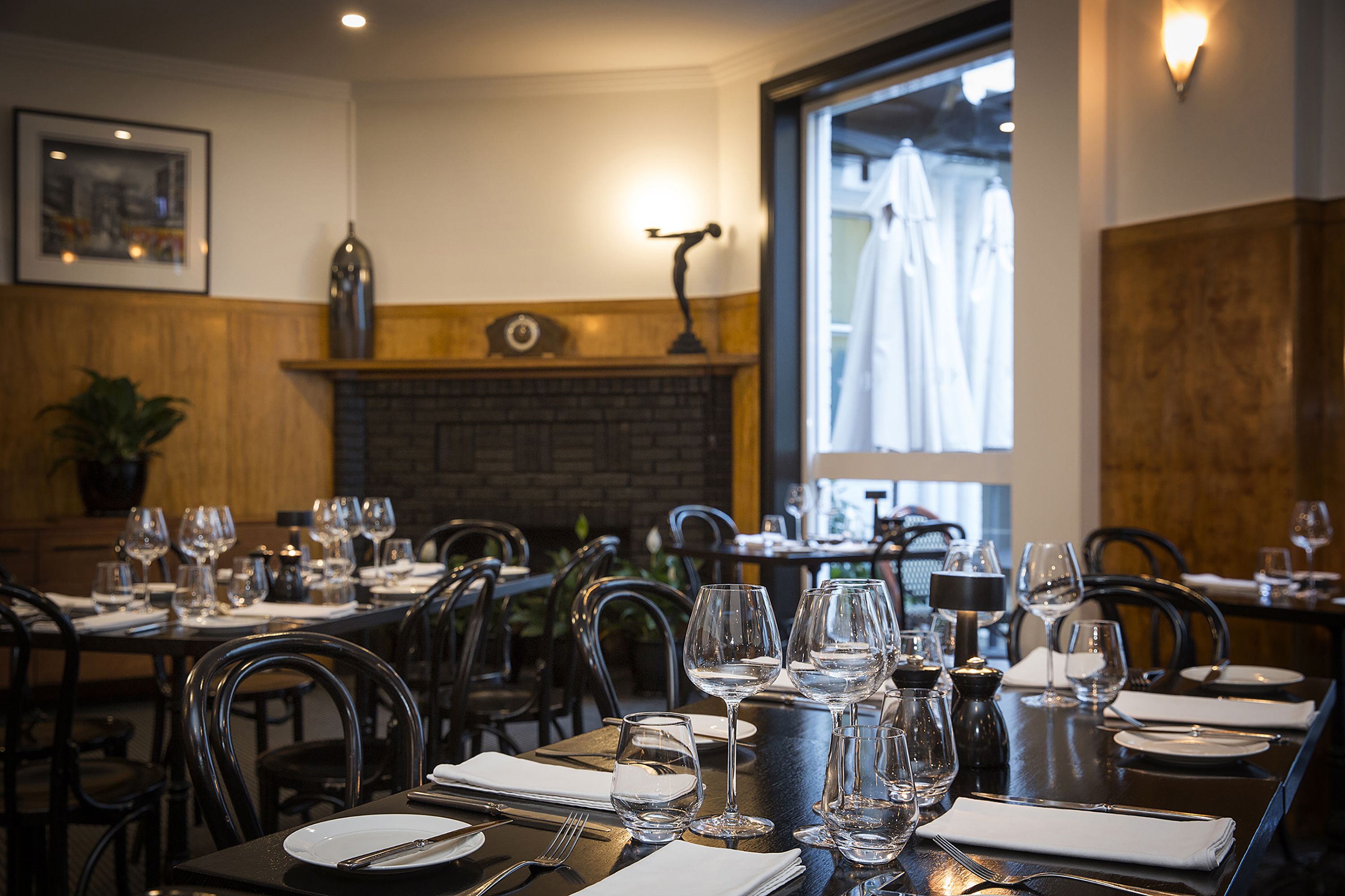 Un restaurant avec des tables dressées pour le service, une cheminée en briques et une vue sur l’extérieur.