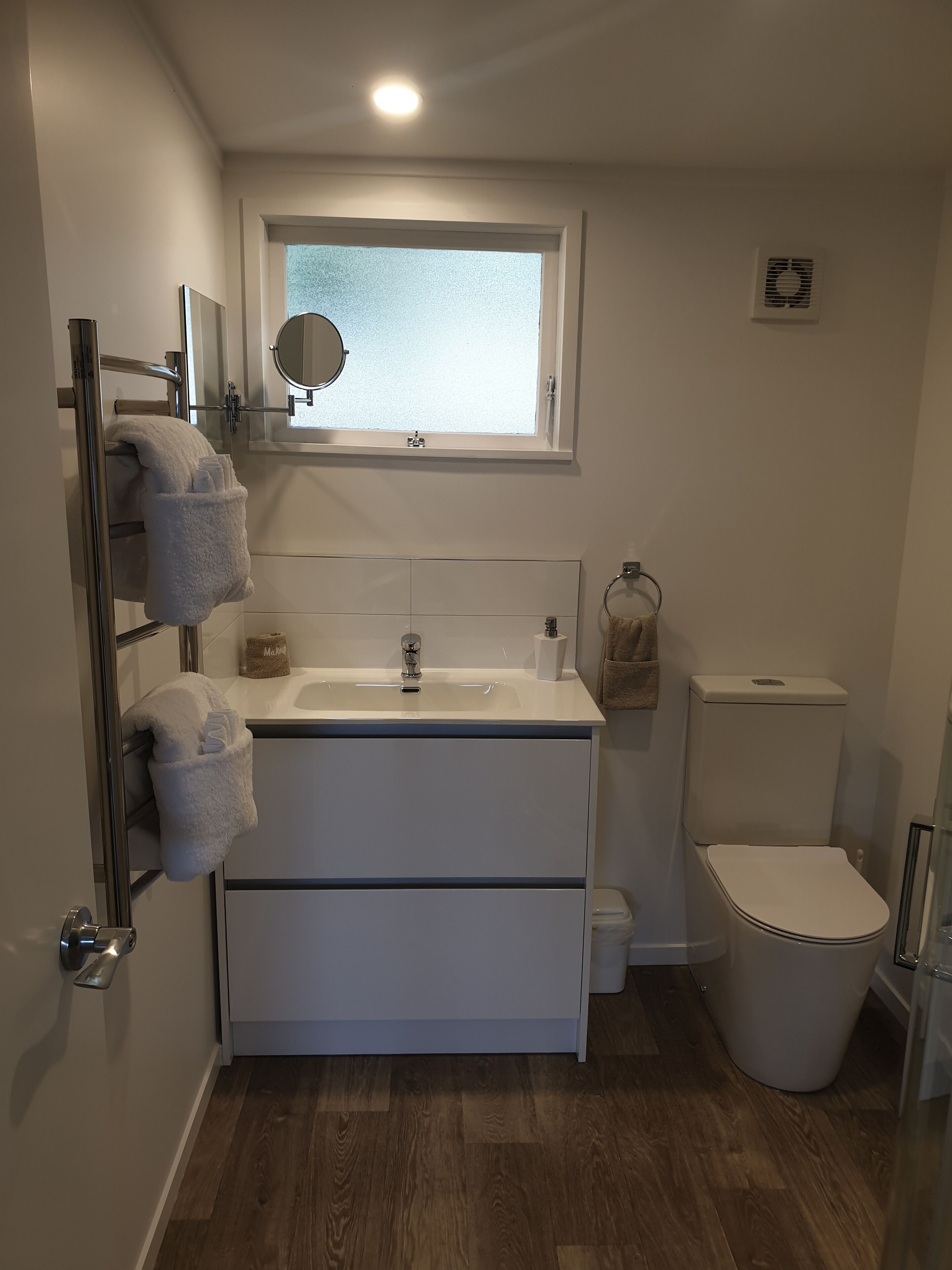A modern bathroom with a white vanity, a mirror above the sink, a toilet, and a window.