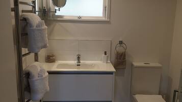A modern bathroom with a white vanity, a mirror above the sink, a toilet, and a window.