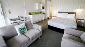A modern hotel room with a sofa, a bed, a small kitchen area, and a dining table. - Little Haven (Taupo)