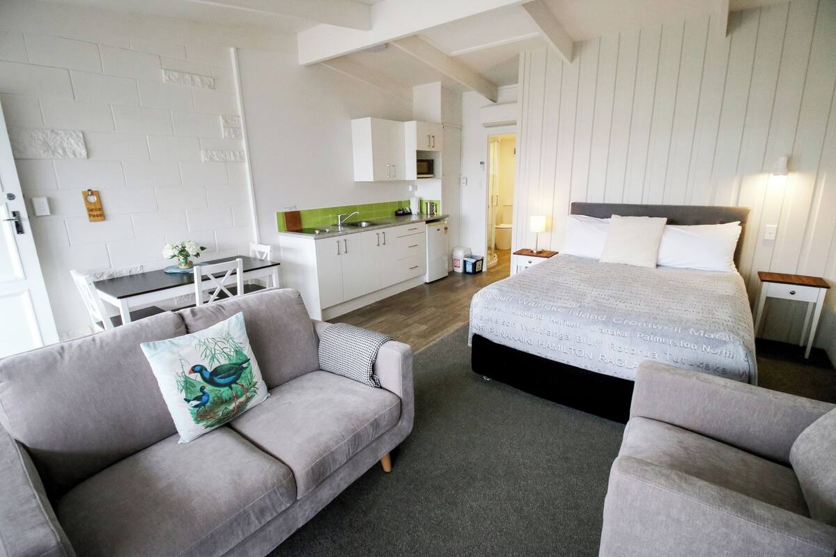Ett modernt hotellrum med en soffa, en säng, ett litet köksutrymme och ett matbord.