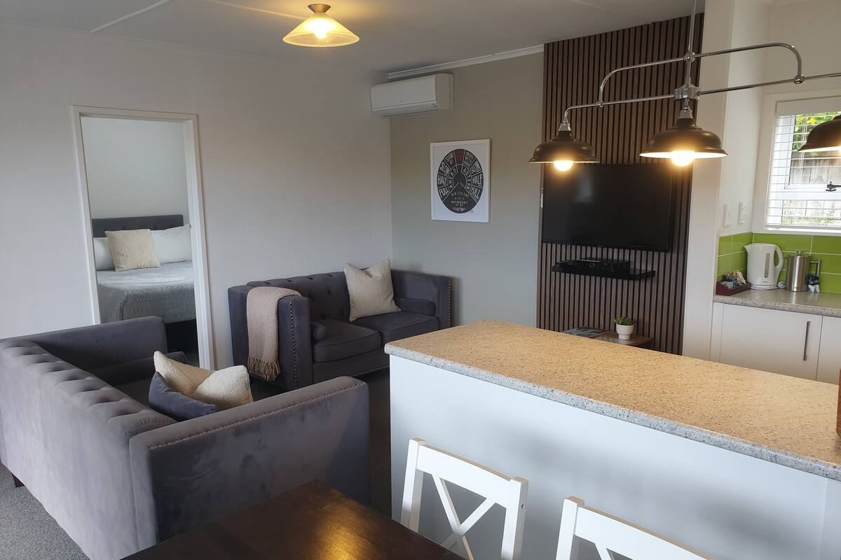 Ett modernt vardagsrum med en soffa, ett matbord och en köksdel med en bänkskiva och skåp.