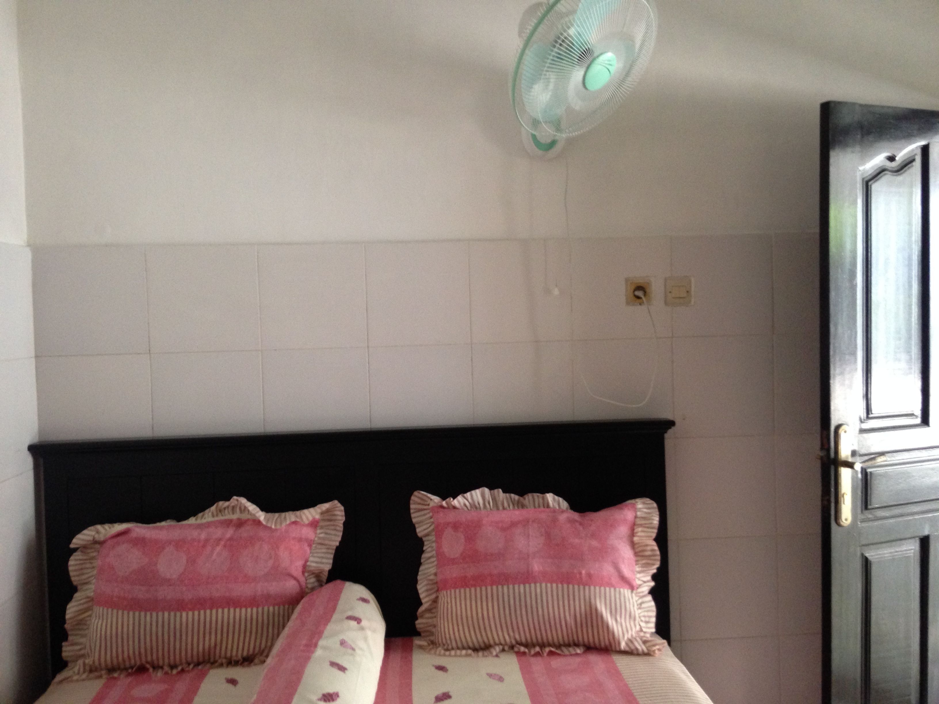 Una habitación con una cama, dos almohadas, un ventilador de pared y una puerta.