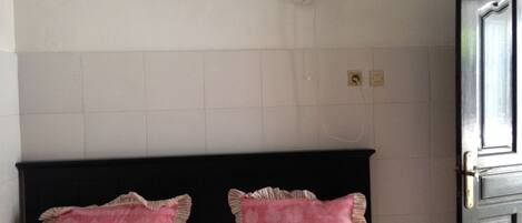 Una habitación con una cama, dos almohadas, un ventilador de pared y una puerta.