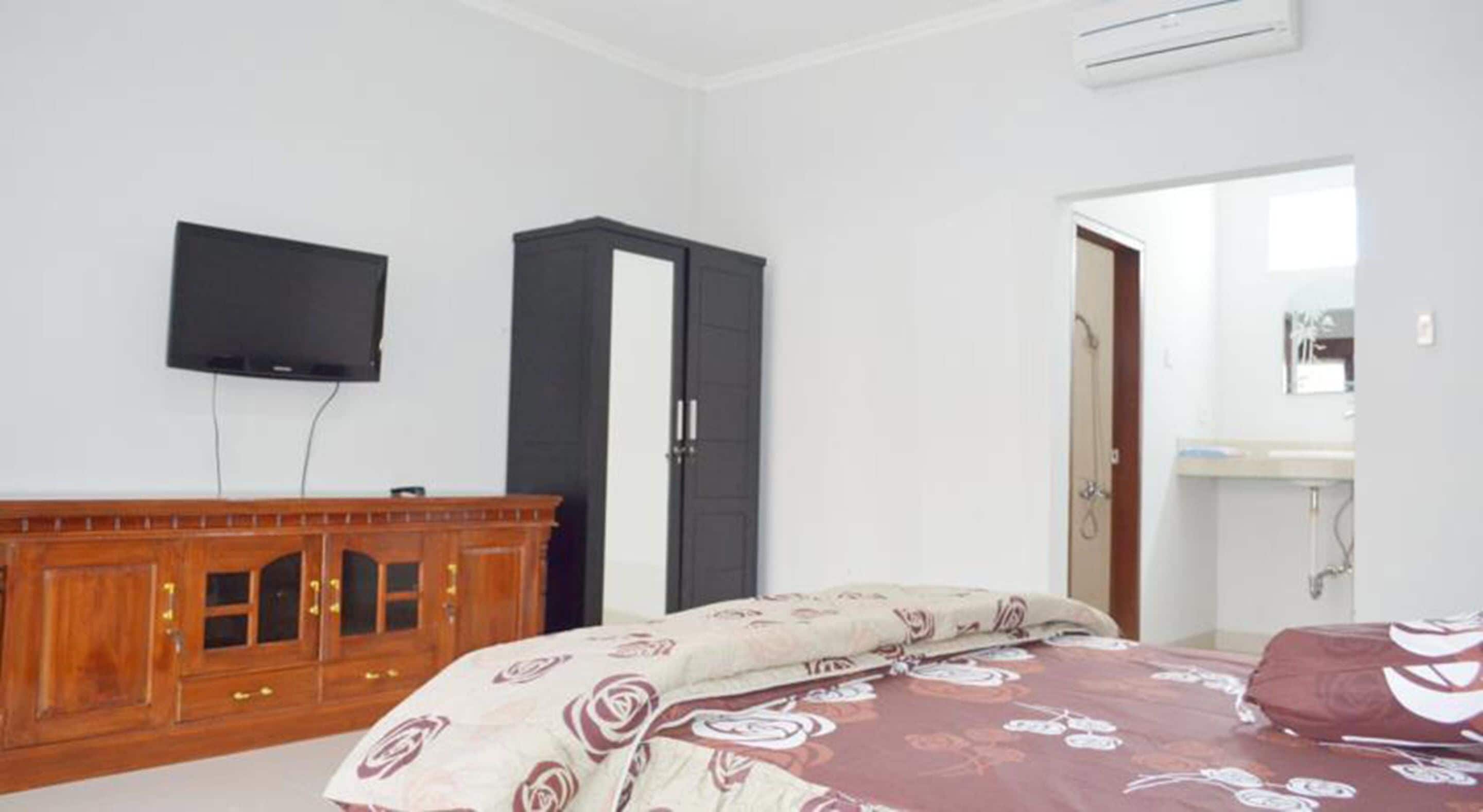 Un dormitorio con cama, armario, televisor y baño visible a través de una puerta abierta.