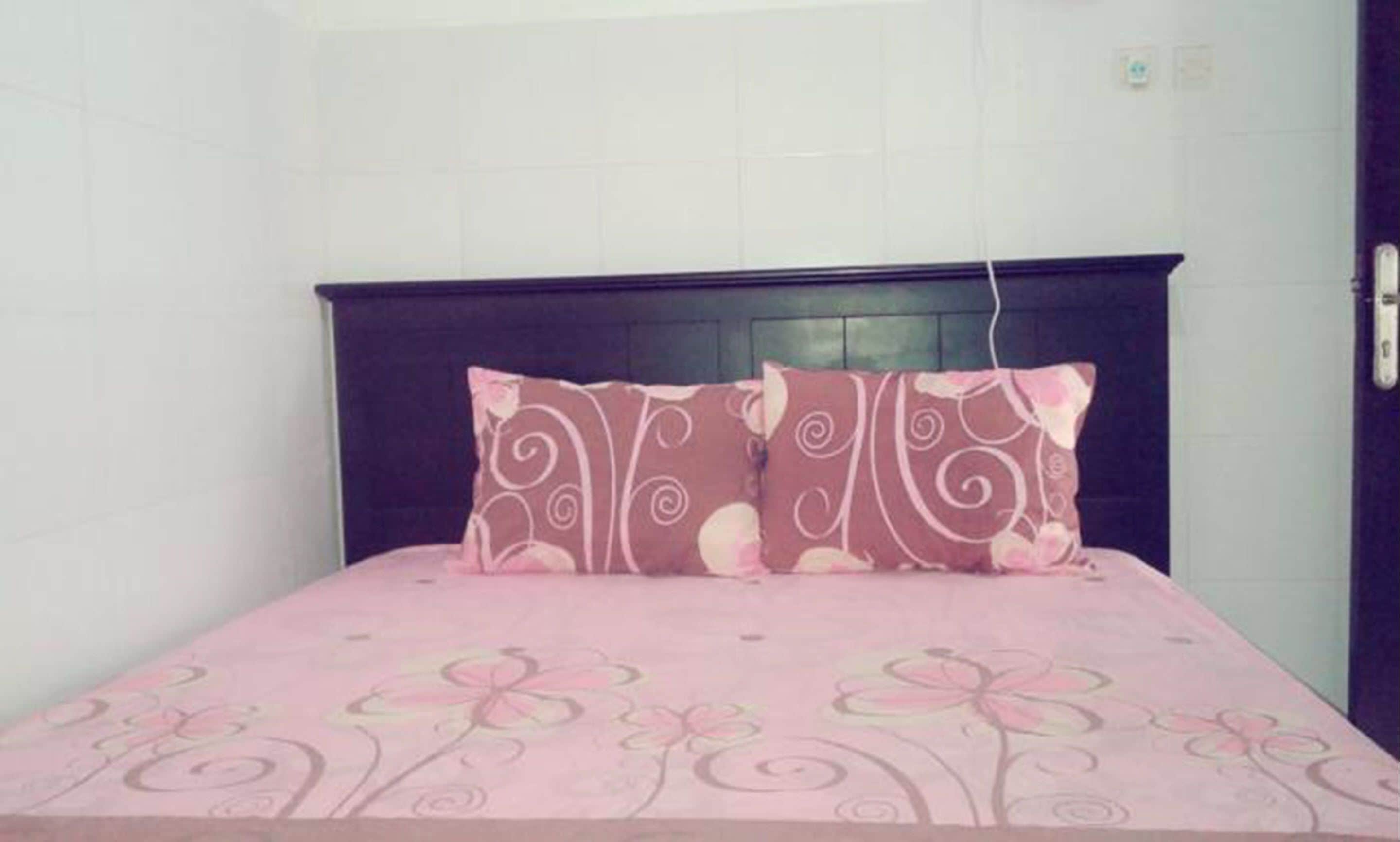 A bed with a dark headboard and a pink floral bedspread.