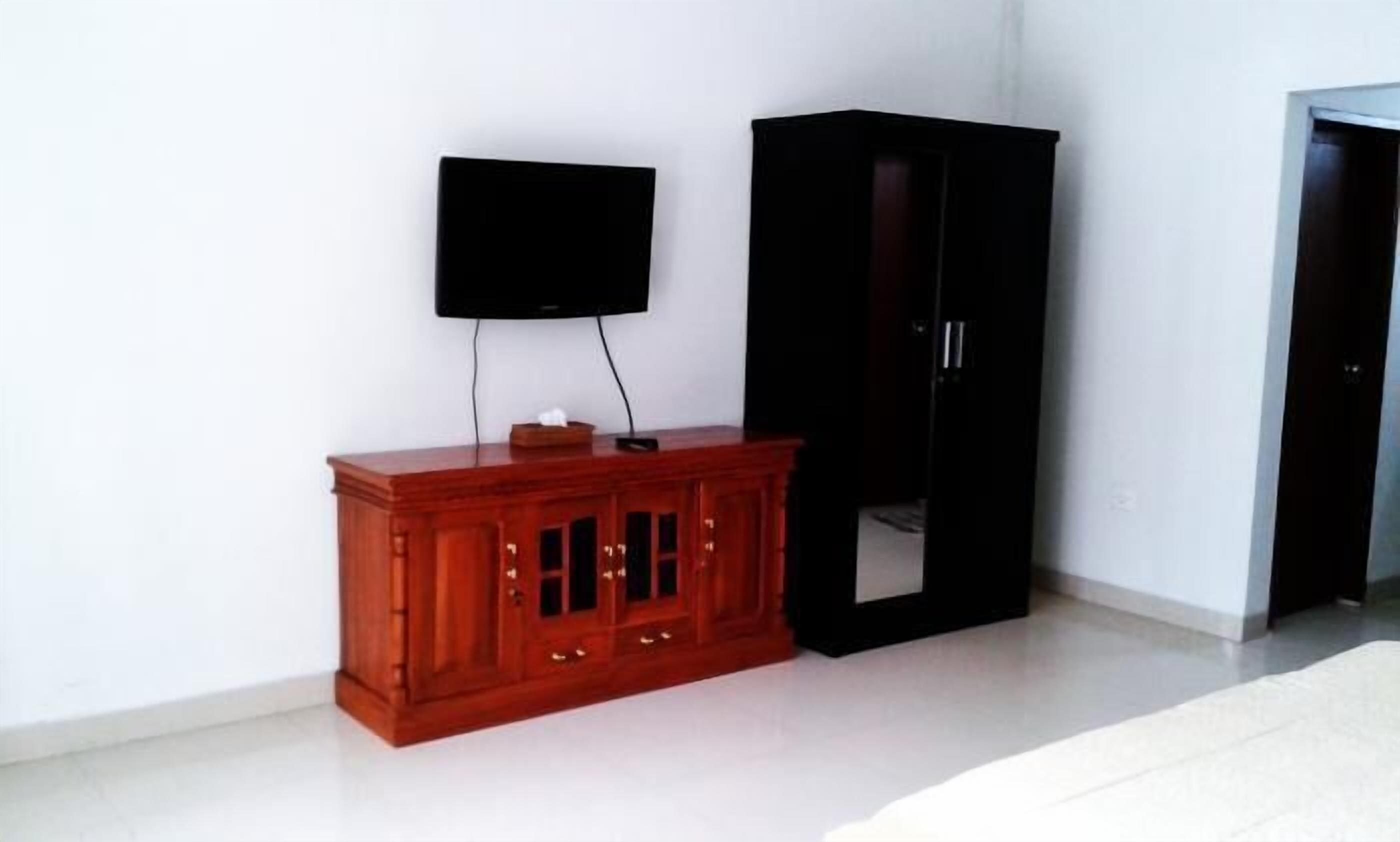 Ein Zimmer mit einem Holzschrank, einem schwarzen Kleiderschrank und einem an der Wand befestigten Fernseher.