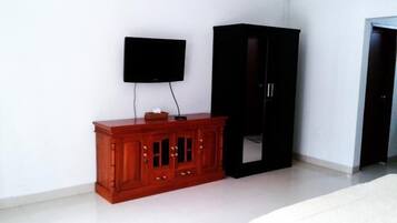 A room with a wooden cabinet, a black wardrobe, and a mounted television.