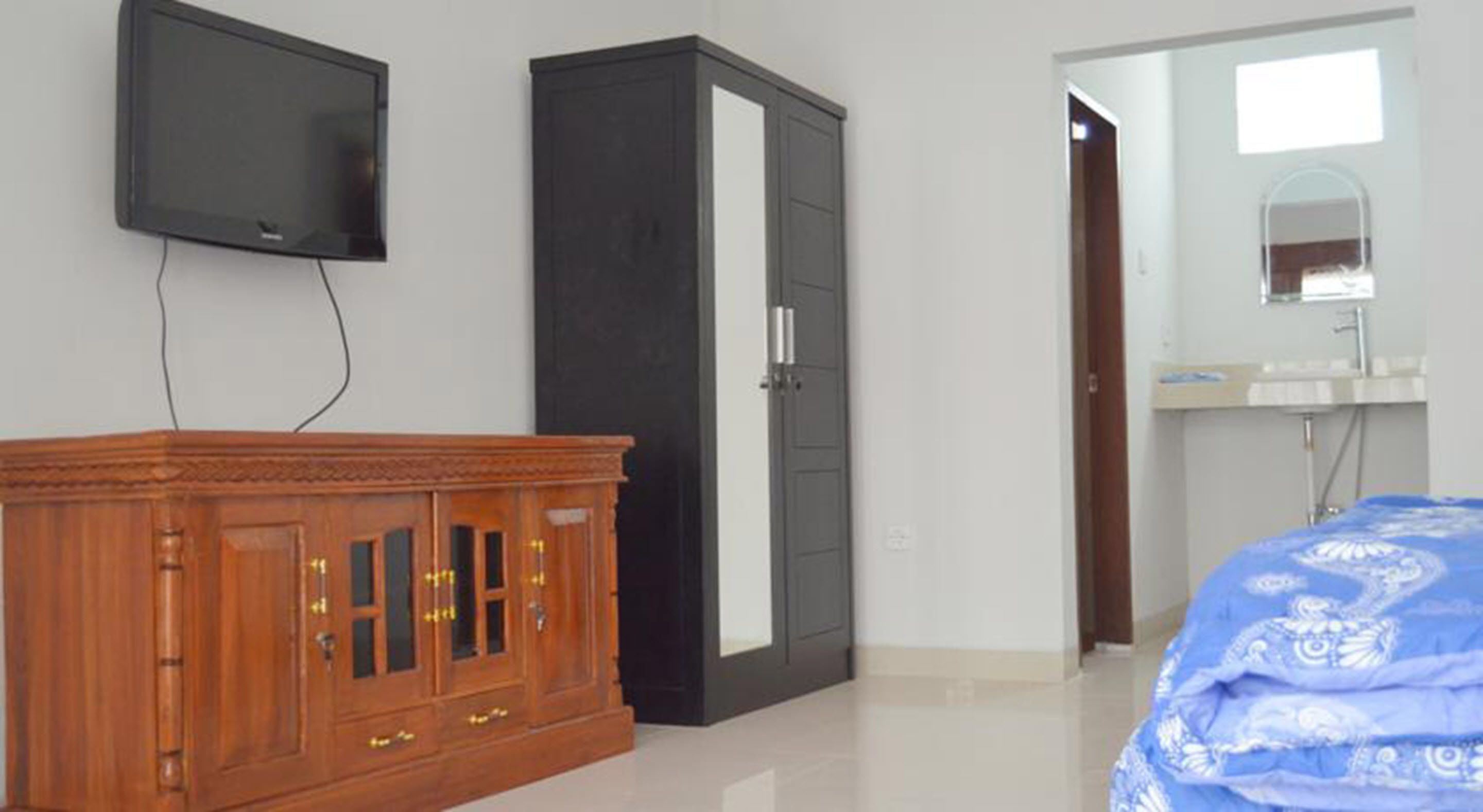 Un dormitorio con un aparador de madera, un armario negro, un televisor montado en la pared y un baño con lavabo y espejo.