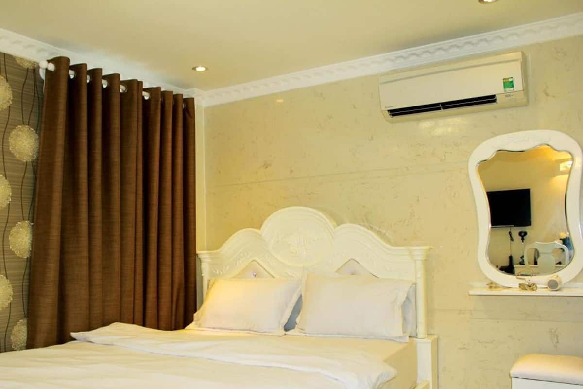 Quarto de hotel com uma cama, uma mesa de cabeceira branca, um espelho e um ar condicionado.