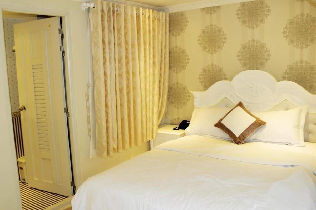 Quarto de hotel com cama, mesa de cabeceira, telefone e porta.