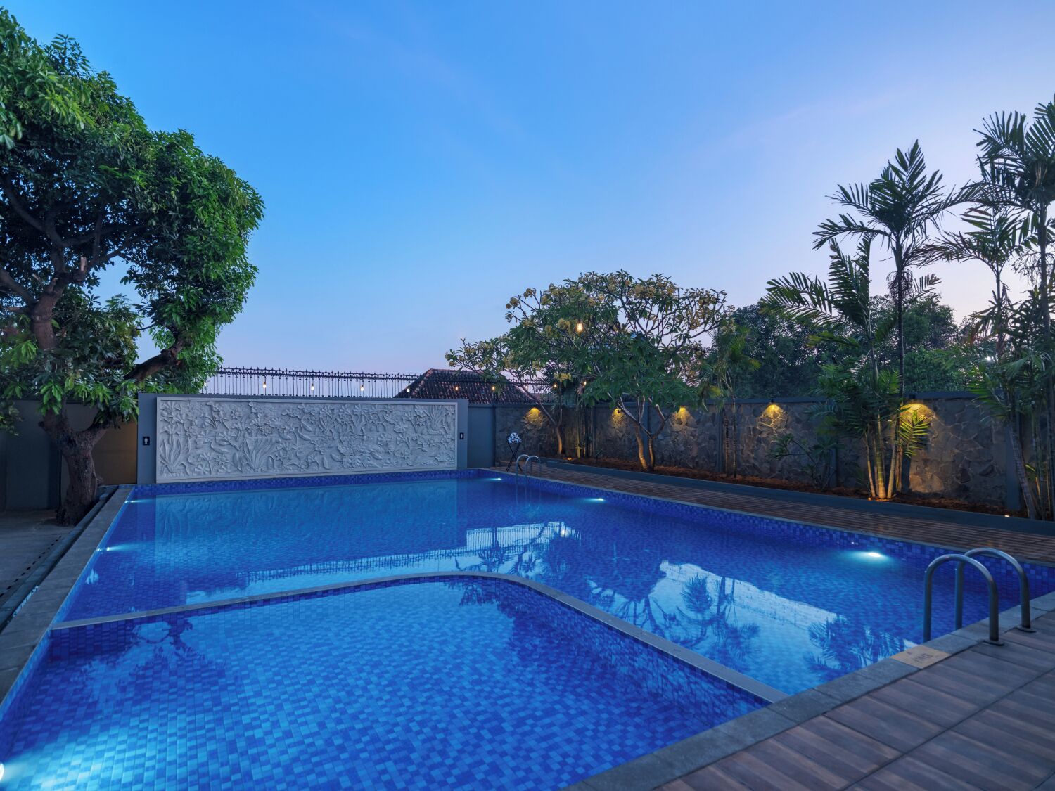 A swimming pool with a tiled edge, surrounded by trees and a stone wall.