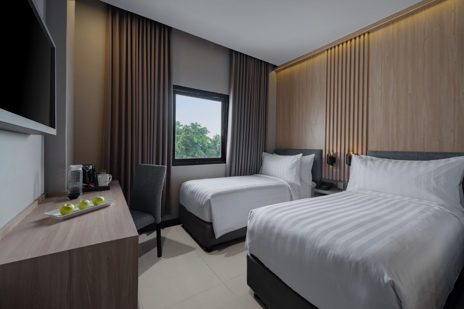 Habitación de hotel con dos camas, un escritorio con cafetera y una ventana con cortinas.