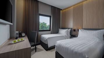 Habitación de hotel con dos camas, un escritorio con cafetera y una ventana con cortinas.
