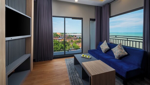 A modern room with a blue sofa, a wooden coffee table, and a large window offering a view of the beach and cityscape. -  Aston Inn Rembang  (Rembang)