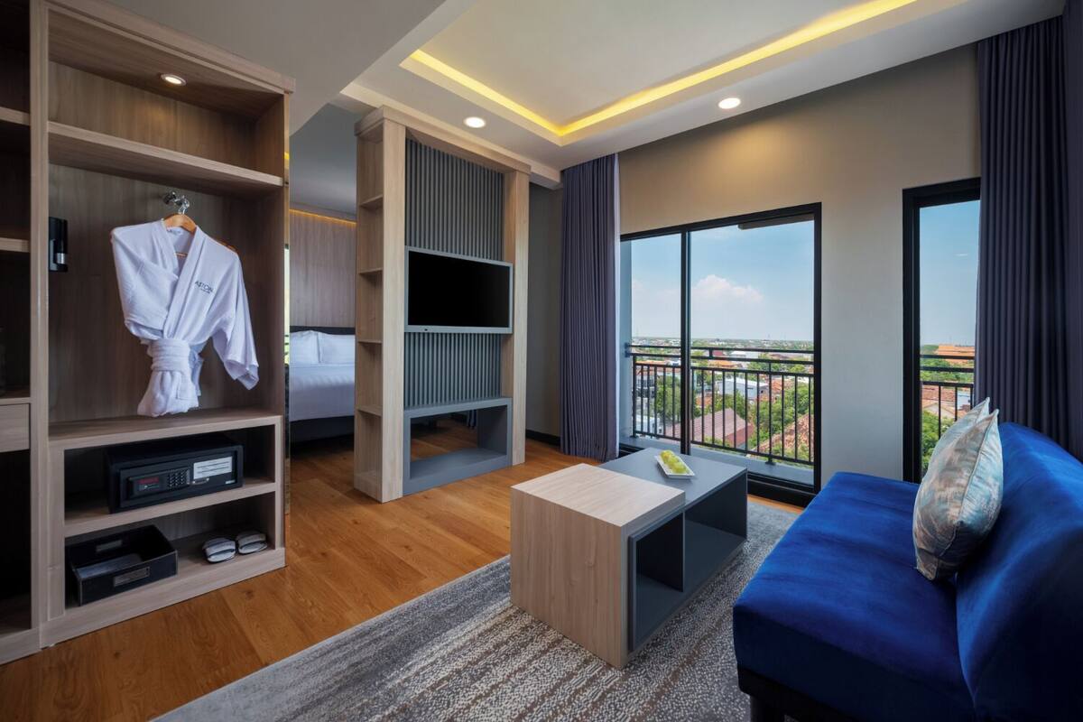 A modern hotel room with a balcony, a TV, a robe, and a coffee table.