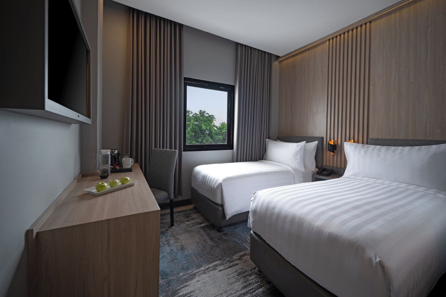 A hotel room with two beds, a desk with a coffee maker, and a window with curtains.