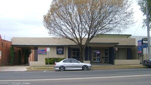 Un motel con zona de estacionamiento techada, un árbol en frente y un coche aparcado en la calle.