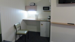 Una kitchenette compacta equipada con microondas, un refrigerador pequeño, una silla y un televisor montado en la pared.