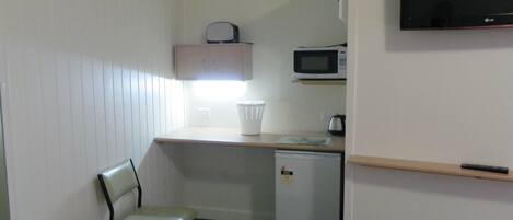 Uma cozinha compacta equipada com micro-ondas, um pequeno frigorífico, uma cadeira e uma televisão fixada na parede.