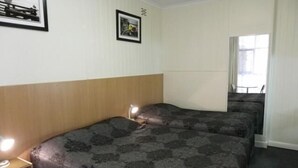 Habitación de hotel con dos camas, cabecera de madera, una mesita de noche con lámpara y cuadros en la pared.