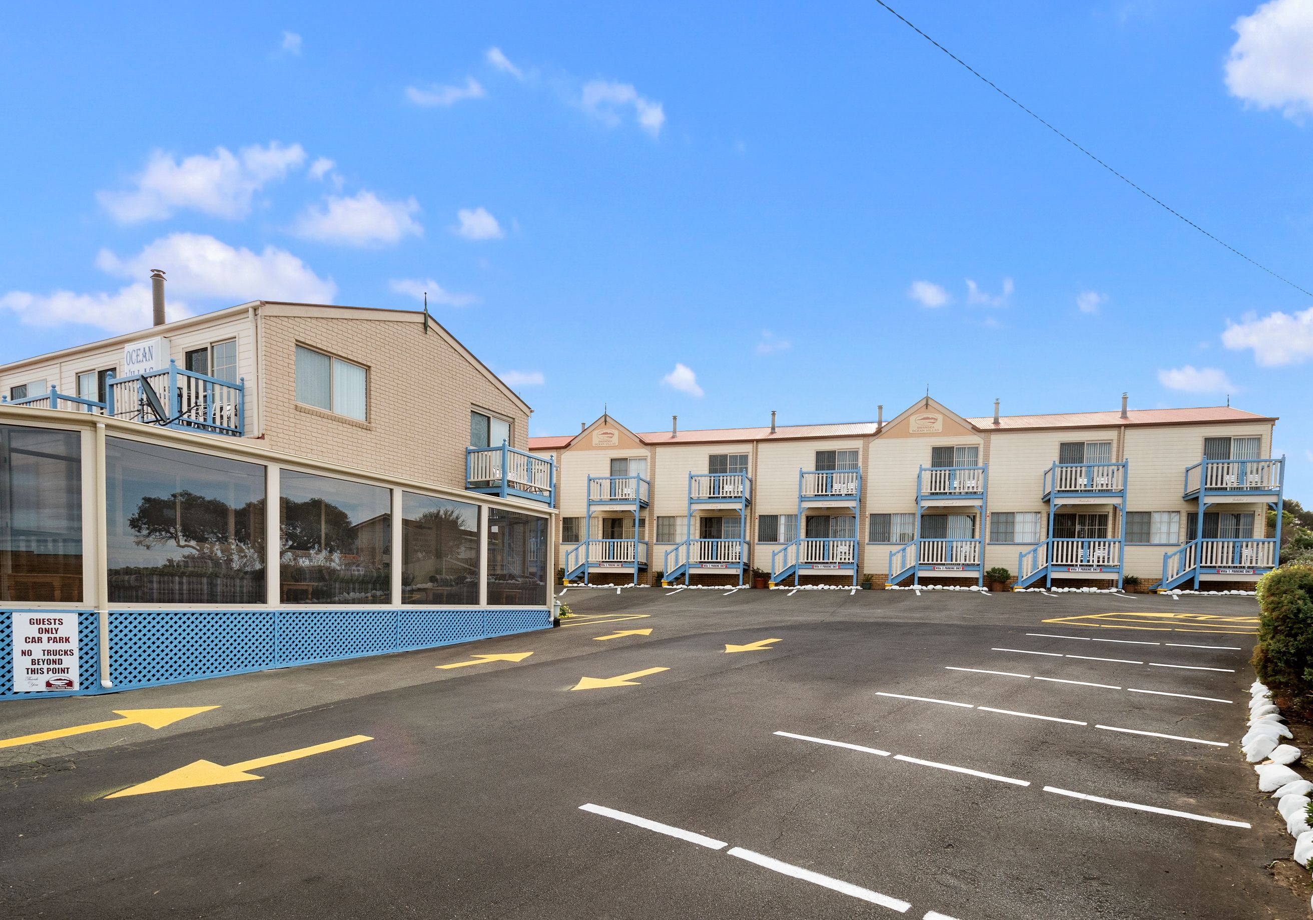 Un motel doté de nombreux balcons, un parking avec des flèches indiquant le sens de circulation et un panneau indiquant qu’il est interdit de stationner les camions.
