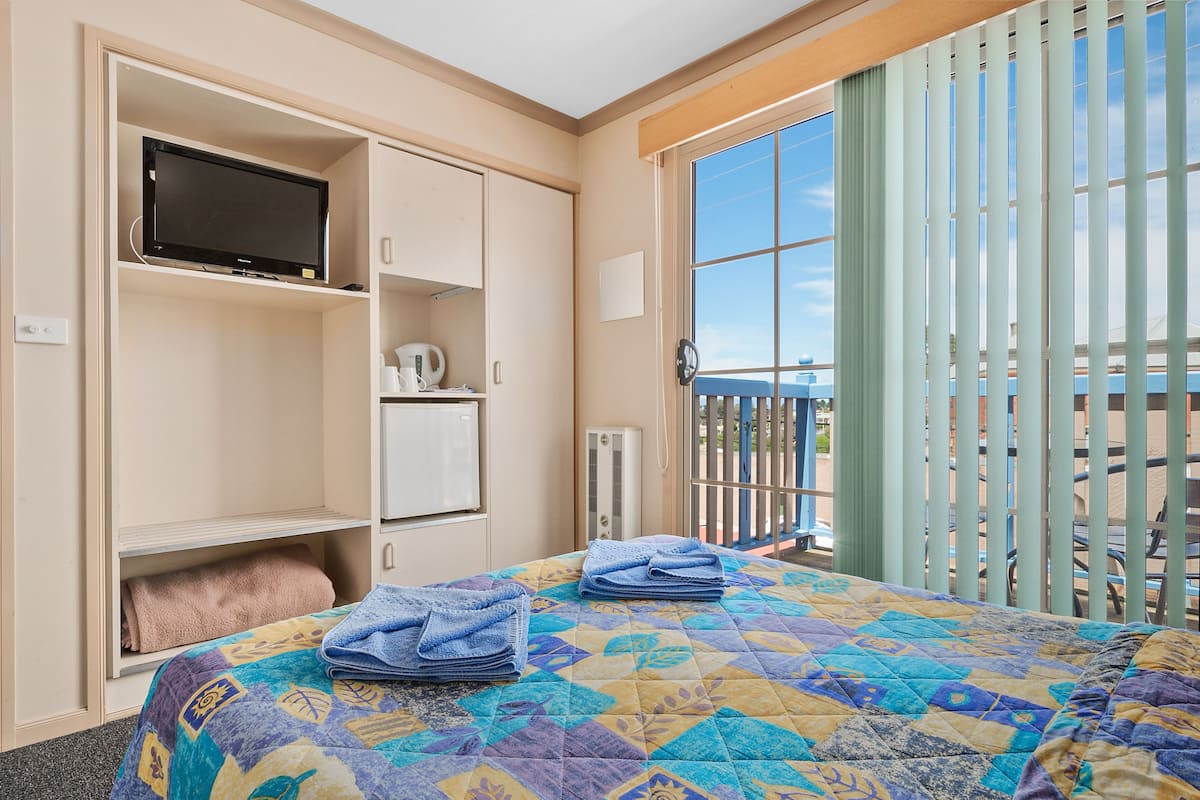 A hotel room with a bed, a television, a kettle, and a view of the outdoors.