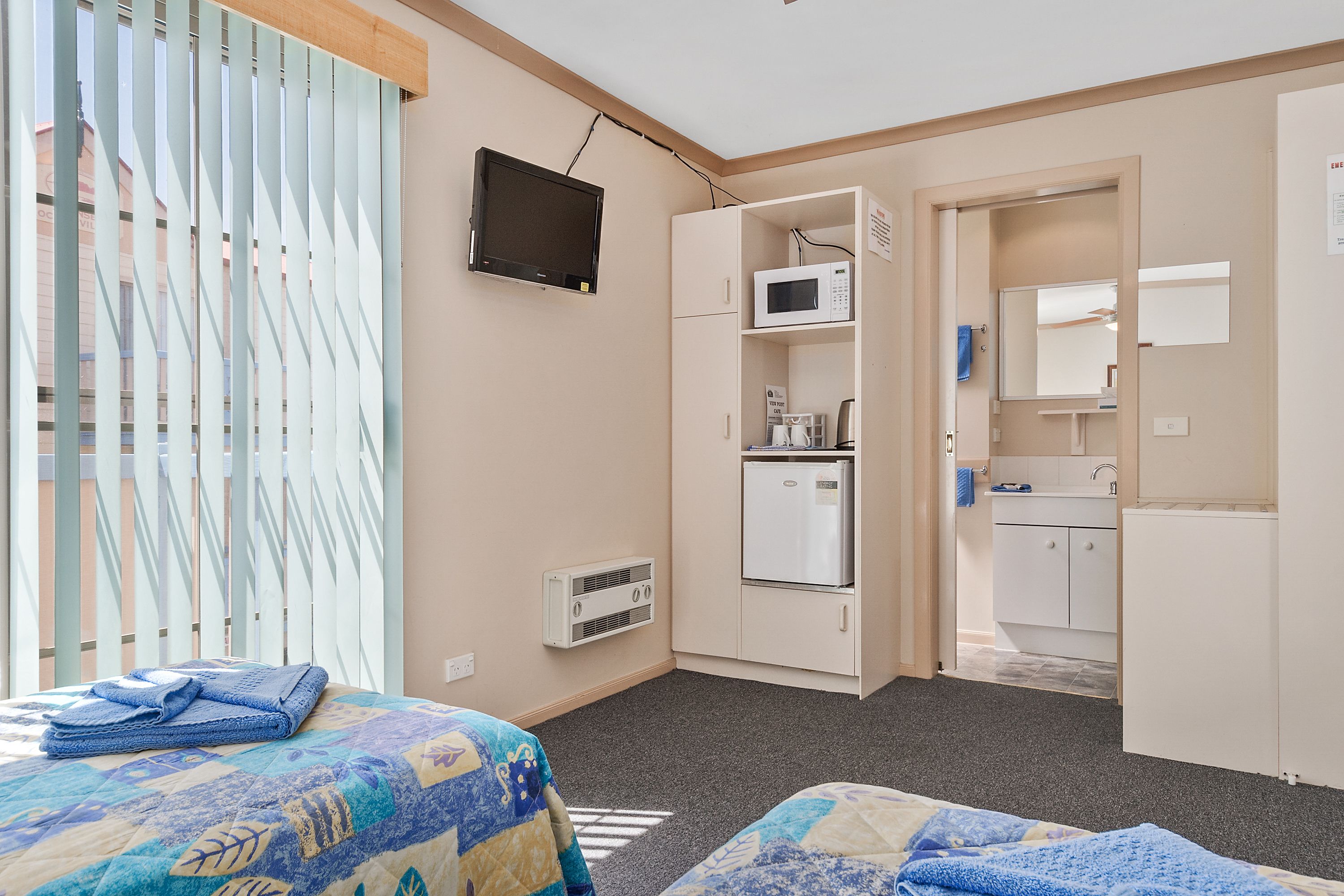 A hotel room with a bed, a TV, a microwave, a refrigerator, and a small kitchenette.