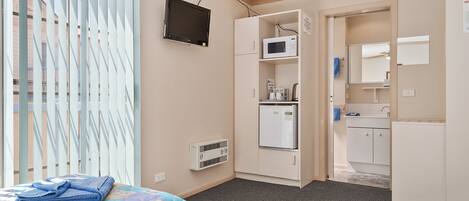 A hotel room with a bed, a TV, a microwave, a refrigerator, and a small kitchenette.