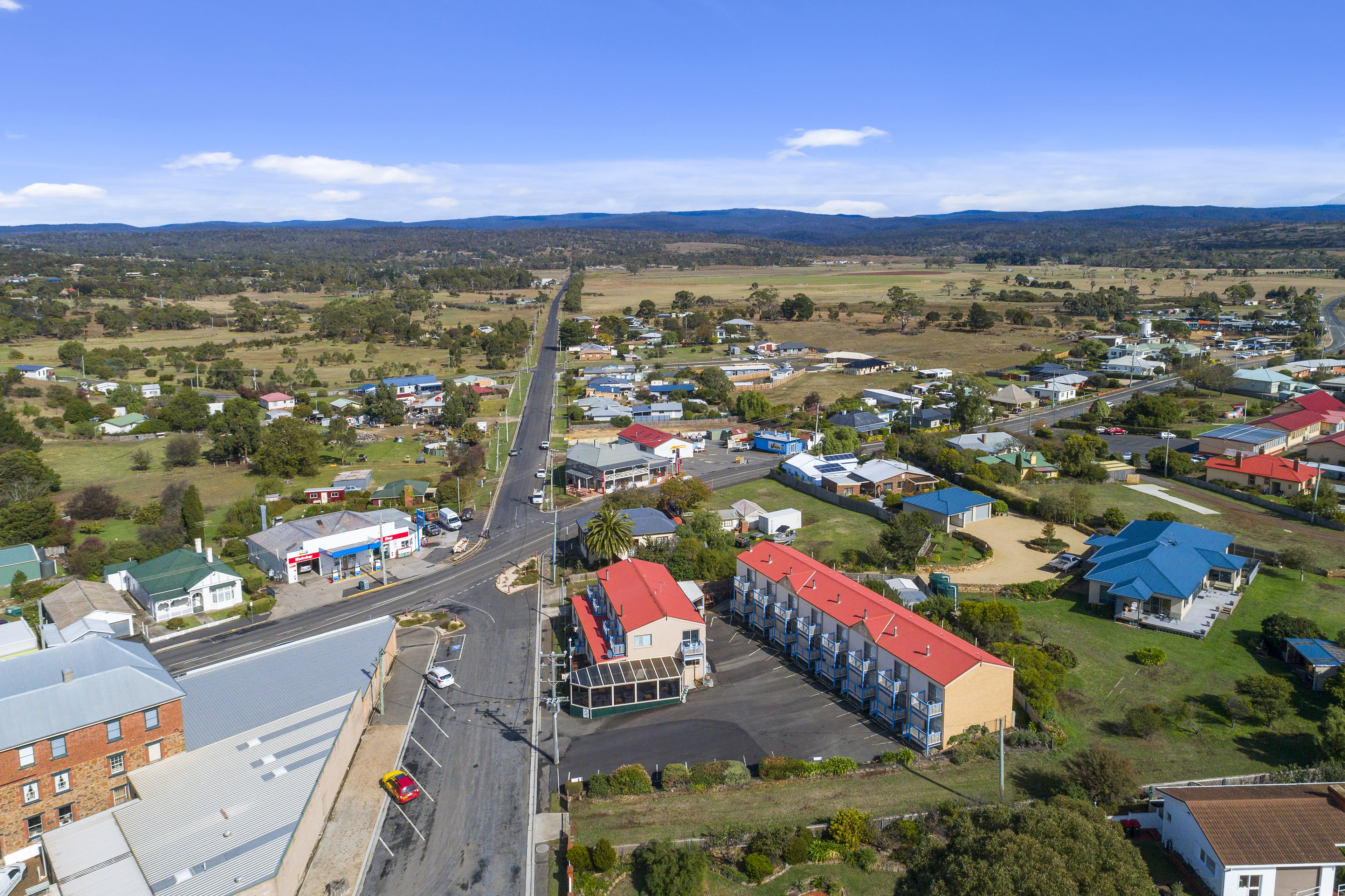 An aerial view of a small town with a main road, residential houses, and a few commercial buildings.