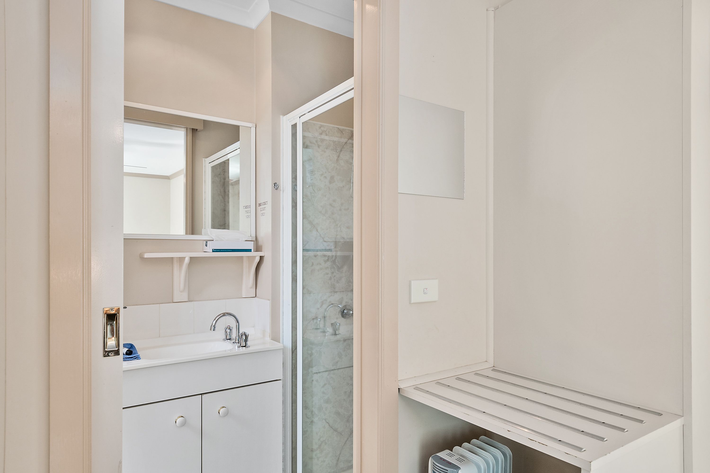 A modern bathroom with a glass shower enclosure, a white sink with a mirror above it, and a built-in shelf below the sink.