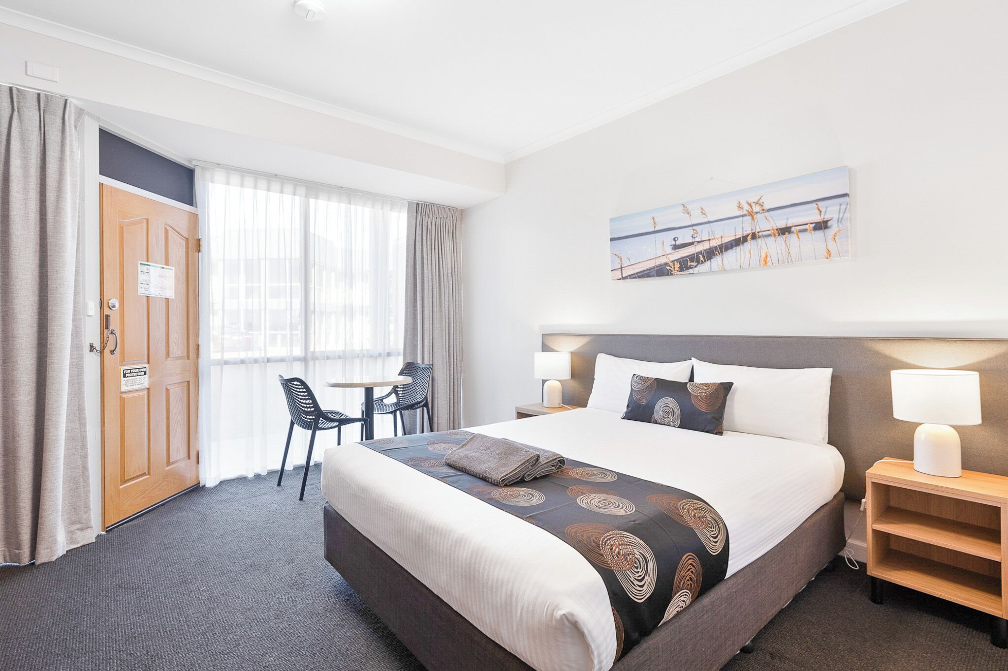Camera d'albergo con un letto grande, una scrivania con sedia, una finestra con tende e un quadro appeso al muro.