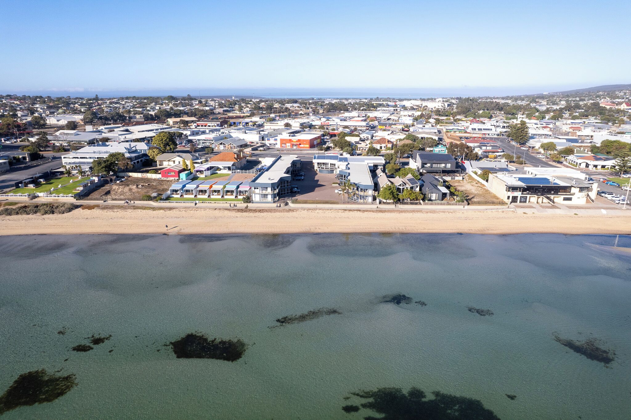 An aerial view of a coastal town with buildings, a beach, and clear skies.