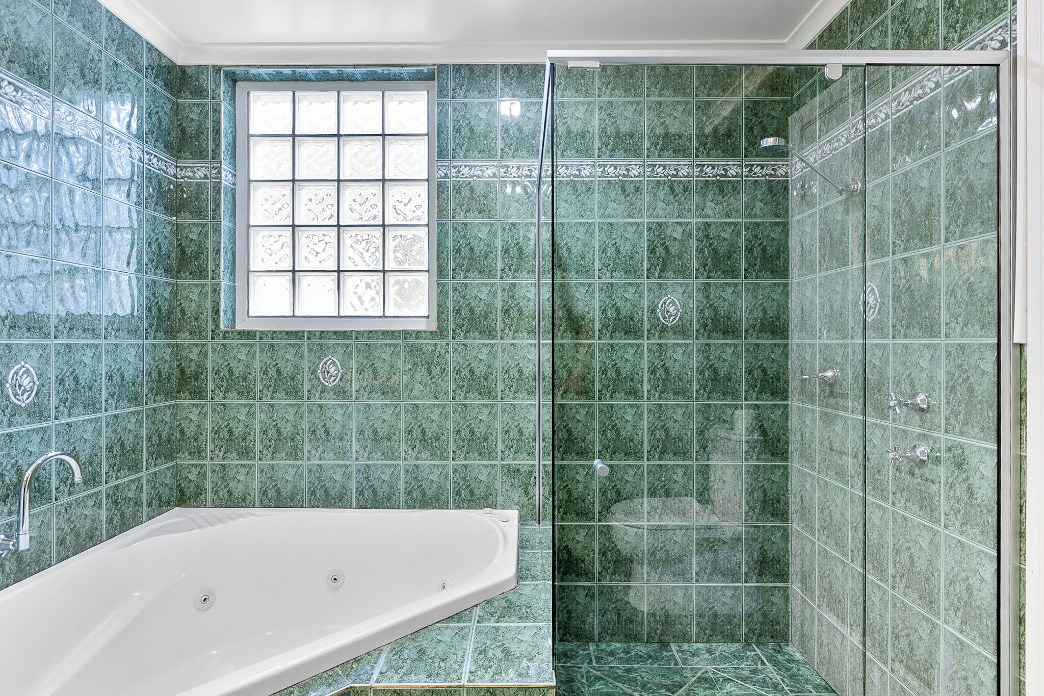 A bathroom with a bathtub, a shower with glass doors, and a window with decorative tiles.