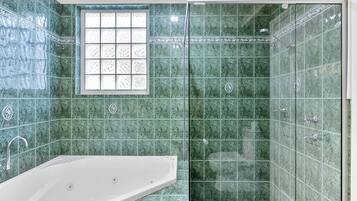 Une salle de bain avec une baignoire, une douche avec des parois en verre et une fenêtre ornée de carreaux décoratifs.