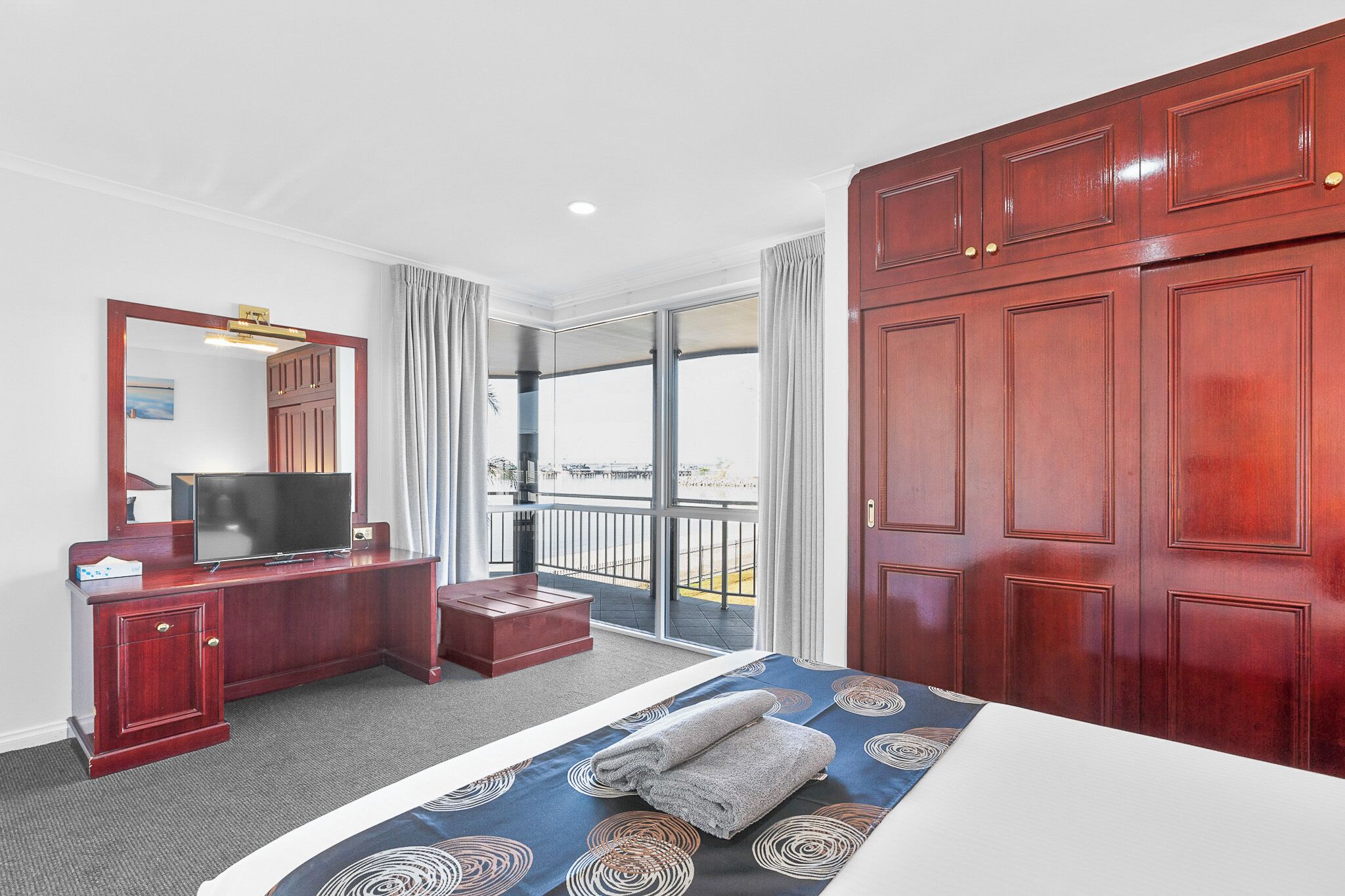 A hotel room with a bed, a desk with a TV, a wardrobe, and a balcony with a view.