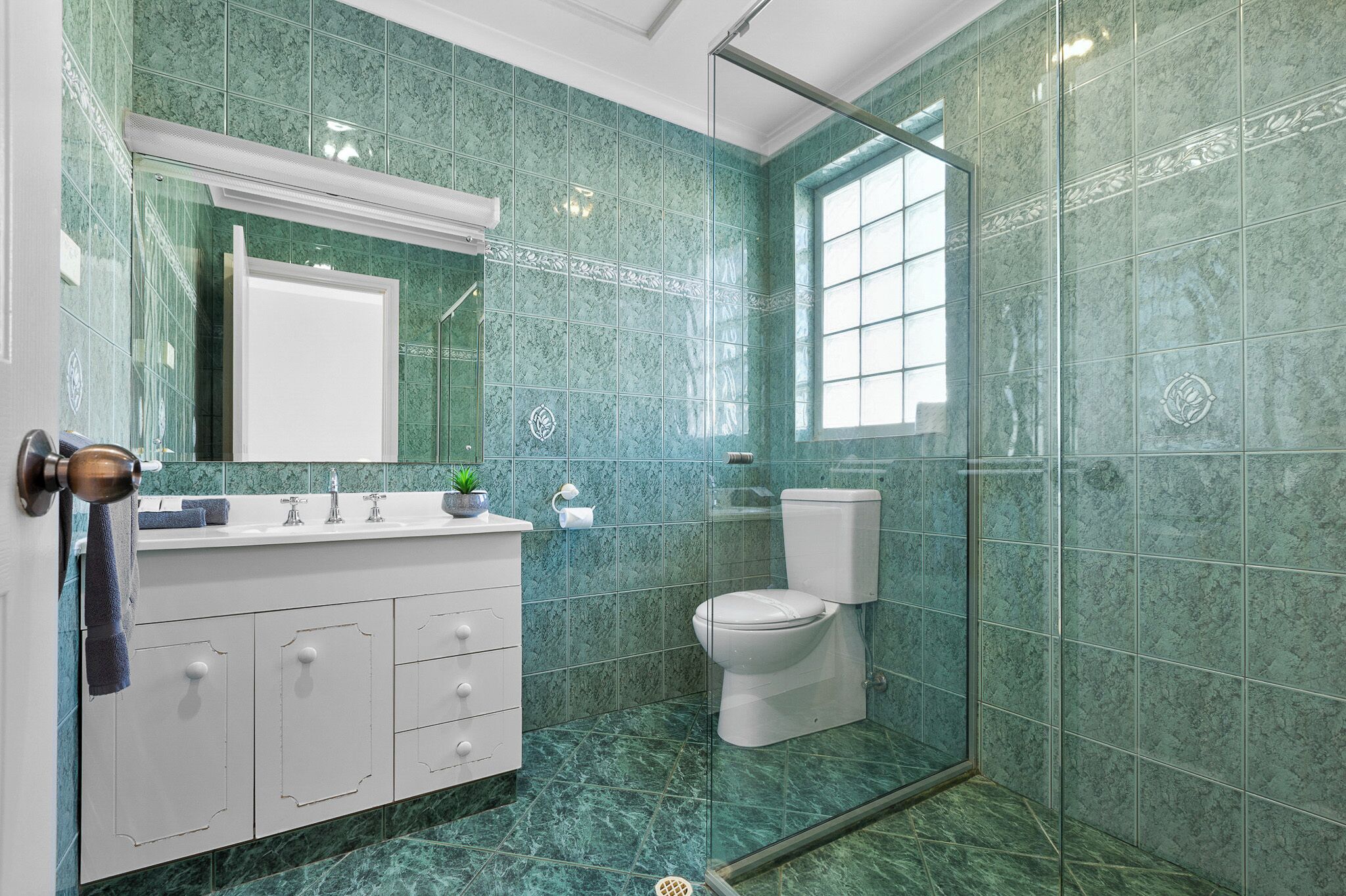 Een badkamer met een wit wastafelmeubel, een douchecabine met glazen wanden en groene marmeren tegels.