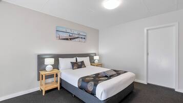 Une chambre d’hôtel avec un lit, deux tables de chevet, une commode, un tableau au mur et une porte.