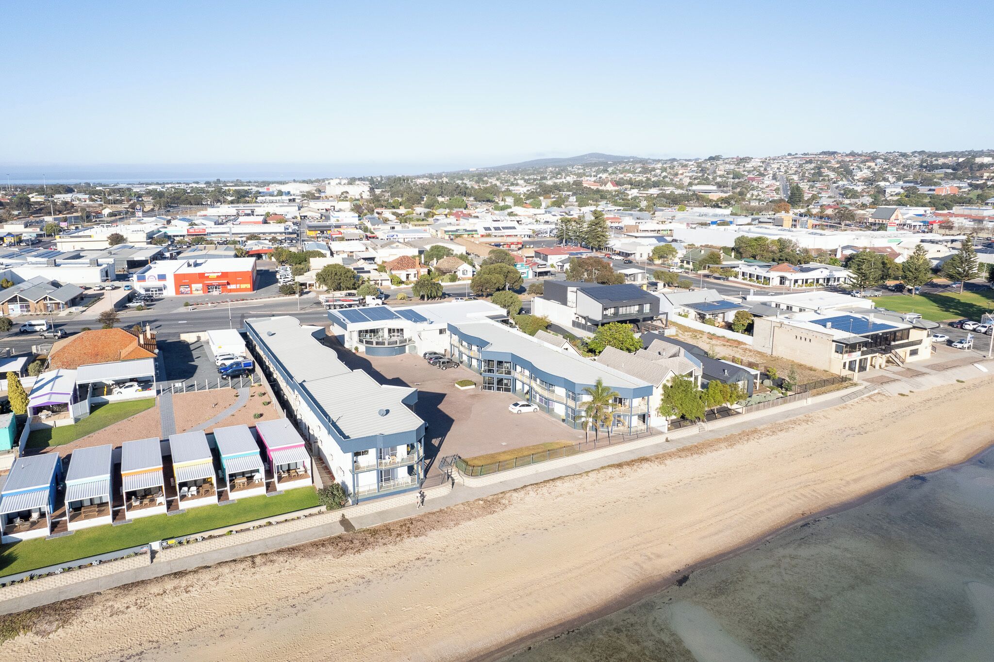Ett flygbildsbild av en kuststad med ett hotell vid stranden, bestående av flera våningar, en sandstrand och en fri utsikt över havet.
